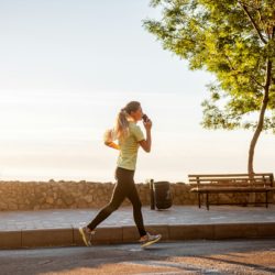 Portrait of young woman in sportswear, jogging in the park by the sea, holding smartphone